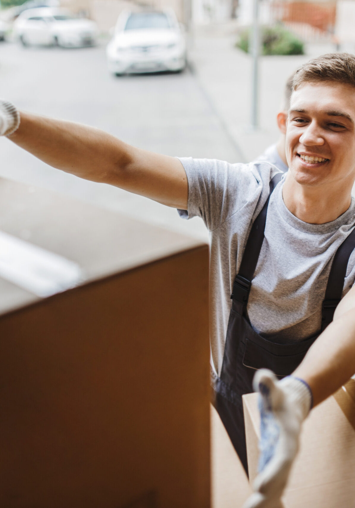 A young handsome smiling mover wearing uniform is reaching for the box while unloading the van full of boxes. House move, mover service.